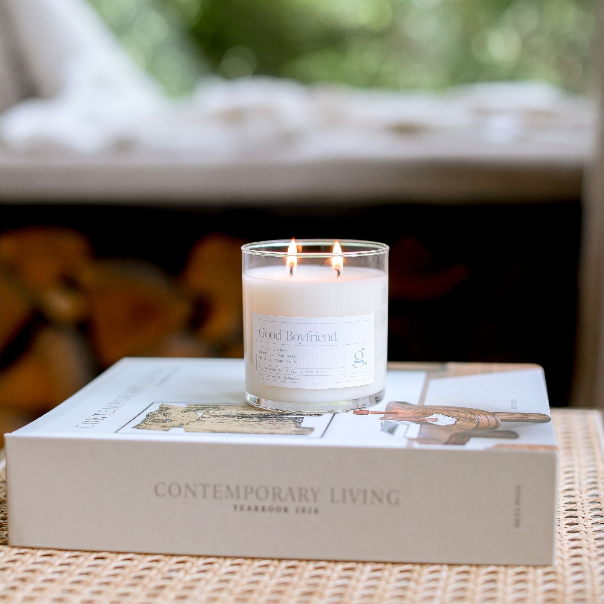 Candle burning on a book titled 'Contemporary Living' on a wooden table outdoors.